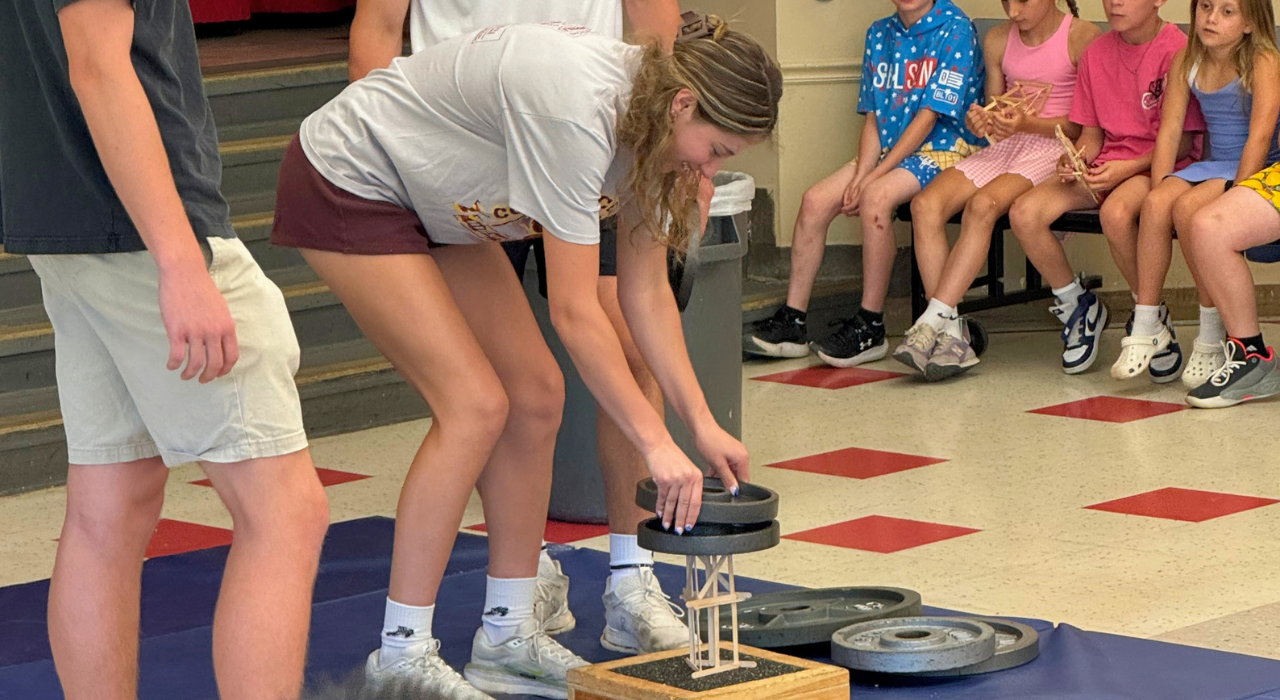A female student stacks free weights on top of a popsicle structure
